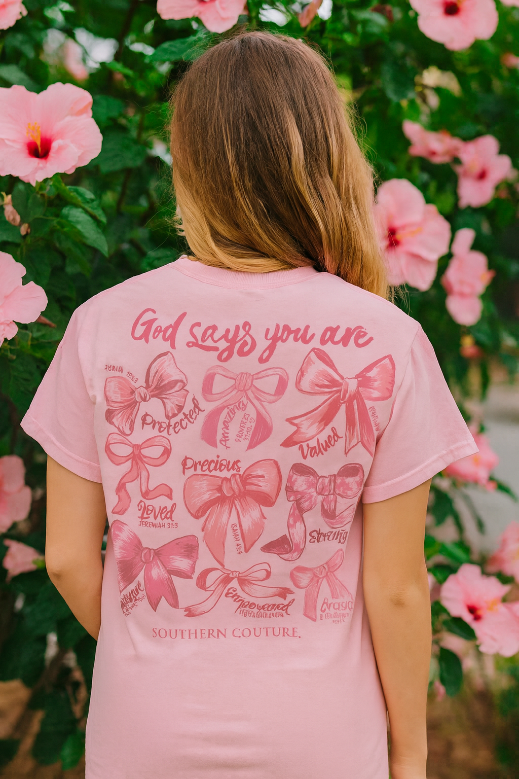 Person wearing a pink t-shirt with decorative bows and text in front of pink flowers